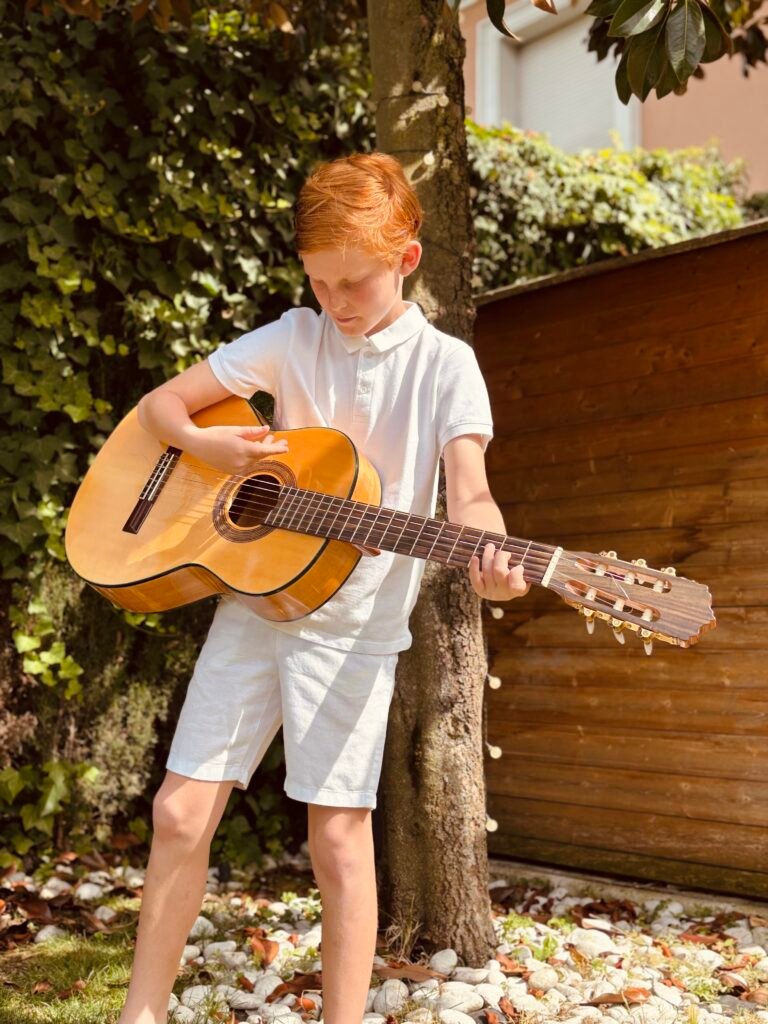 Young boy in white playing a classical guitar in a garden