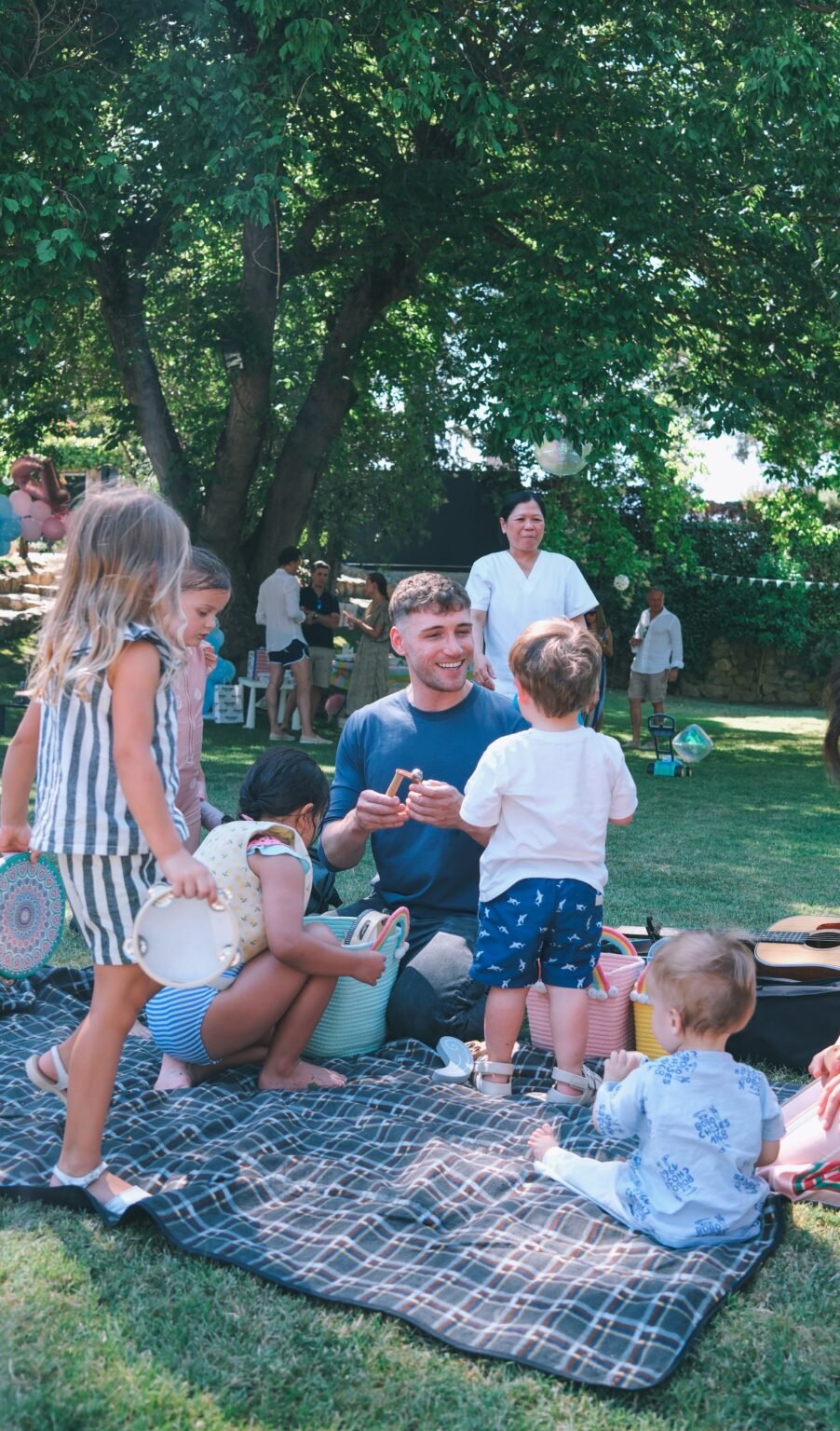 Pop-up class in the park: teacher in a blue t-shirt playing music with young children